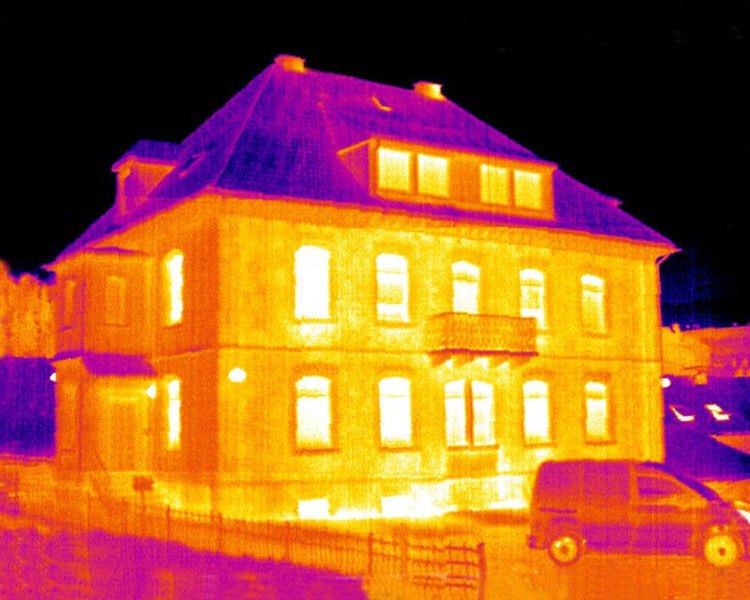 Termografibild av ett bostadshus där värmeförluster syns som gula och vita partier runt fönster och grund