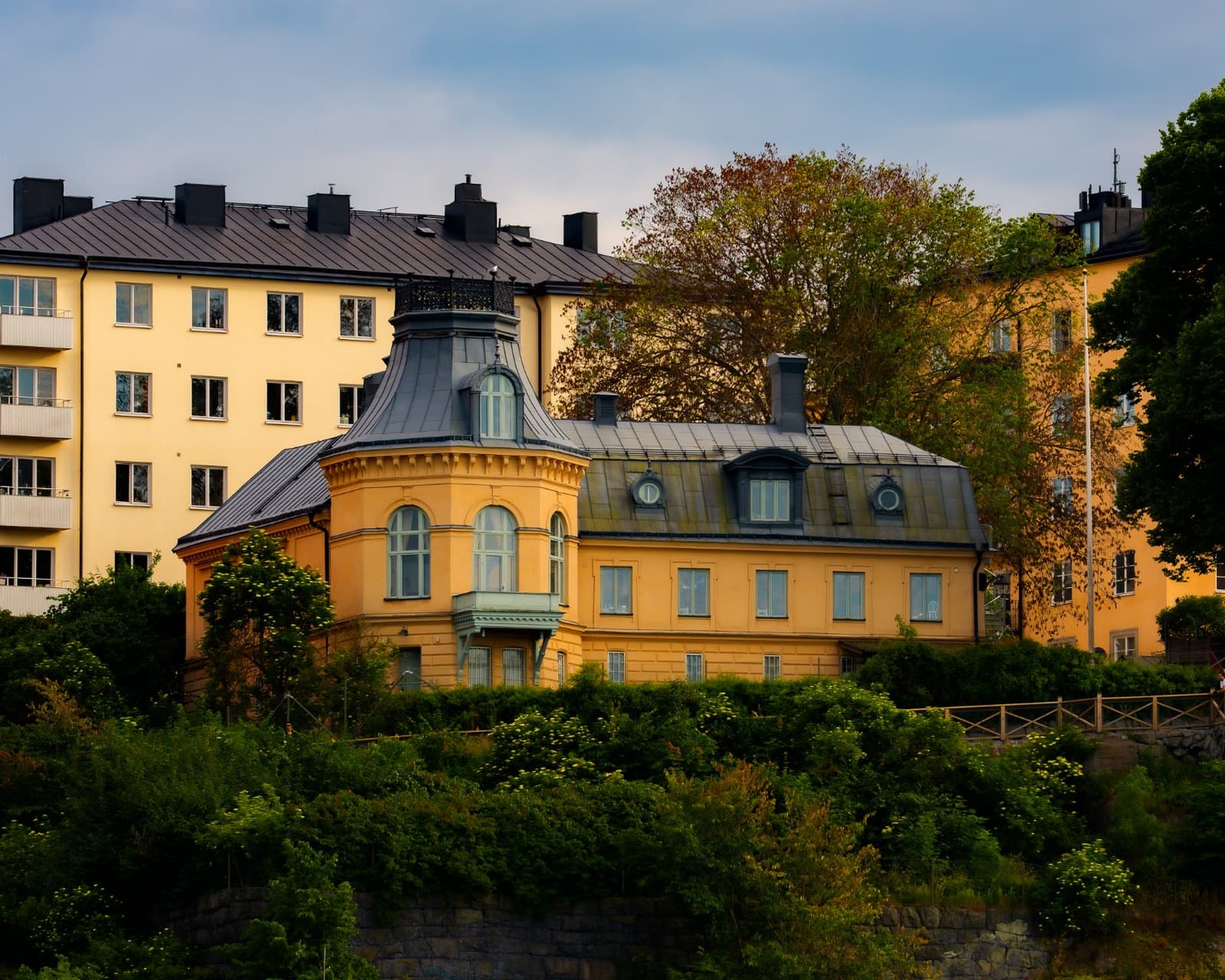 Gul panelbyggnad på en klippa omgiven av grönska i Stockholm